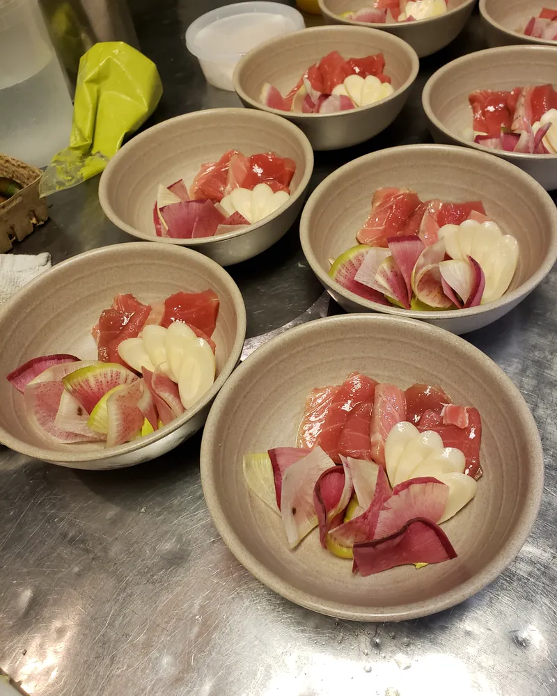 Rows of small bowls of crudo being prepared for an event
